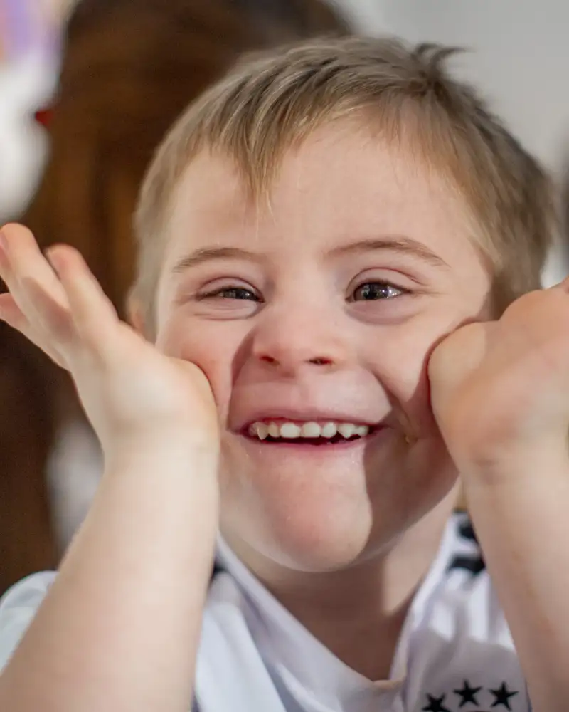 Ein kleiner Junge hält beide Handflächen an seine Wangen und lacht.