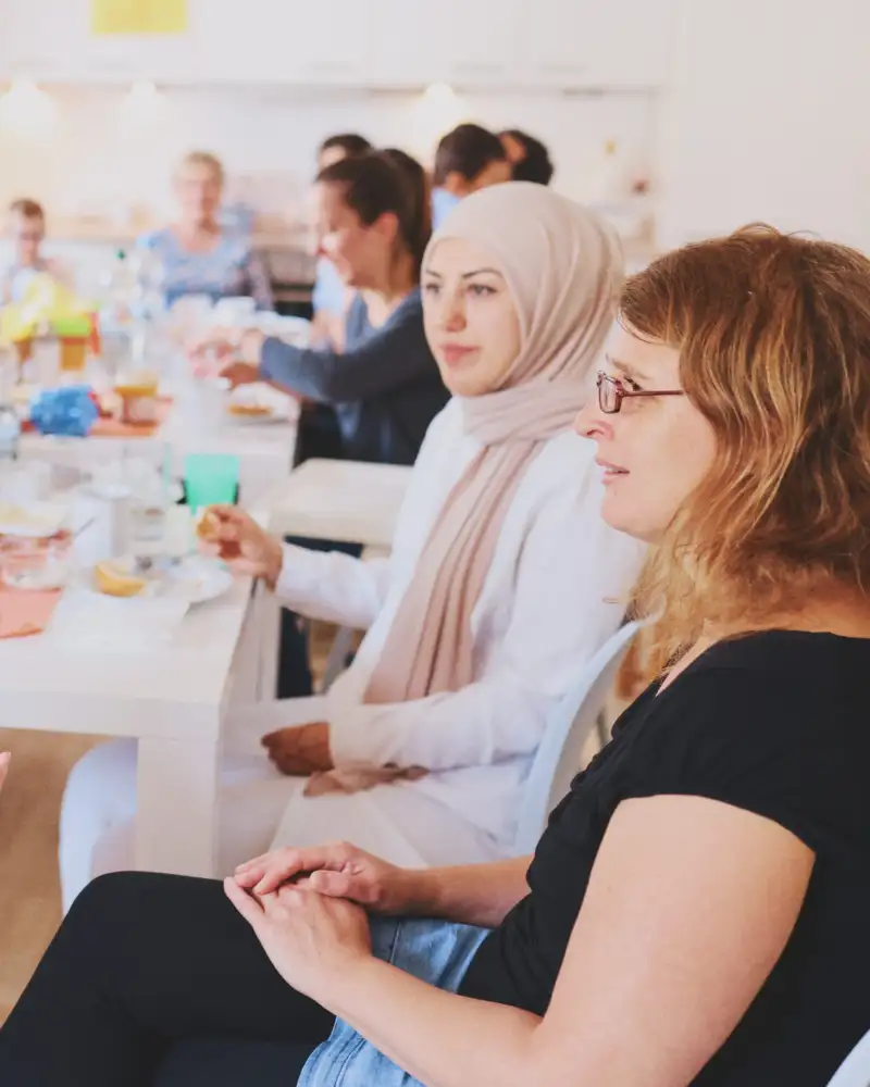 Viele Frauen mit und ohne Migrationshintergrund sitzen an einem langen gedeckten Tisch und sprechen miteinander.