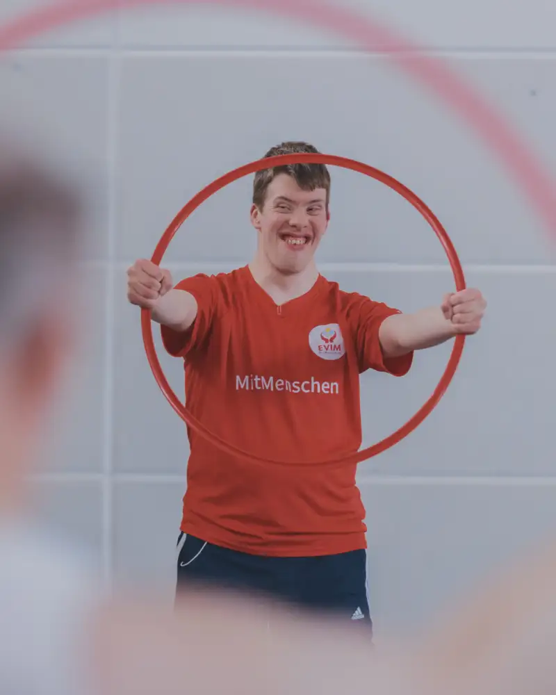 Ein junger Mann mit Downsyndrom hält einen Hula Hoop Reifen in die Höhe