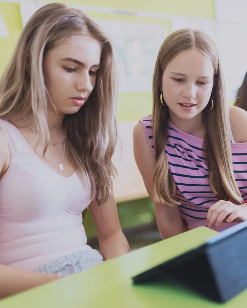 Zwei junge Mädchens schauen in einem Klassenzimmer gemeinsam auf ein Tablet