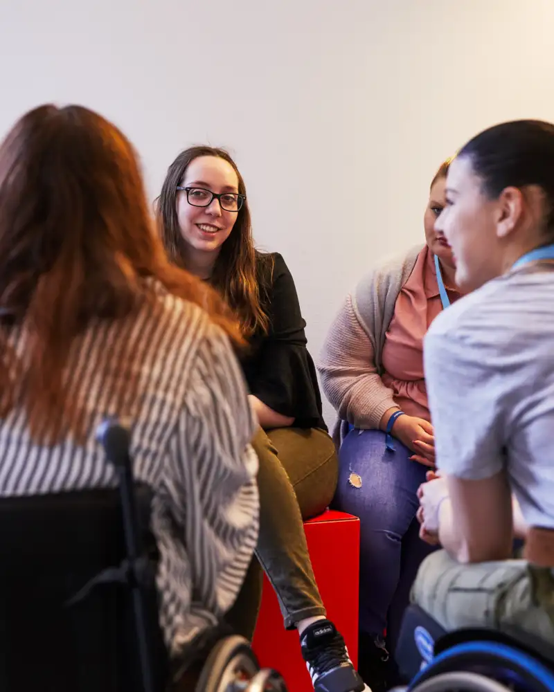 Eine Gruppe junger Frauen bildet einen Gesprächskreis. Zwei von ihnen sitzen erkennbar im Rollsruhl.