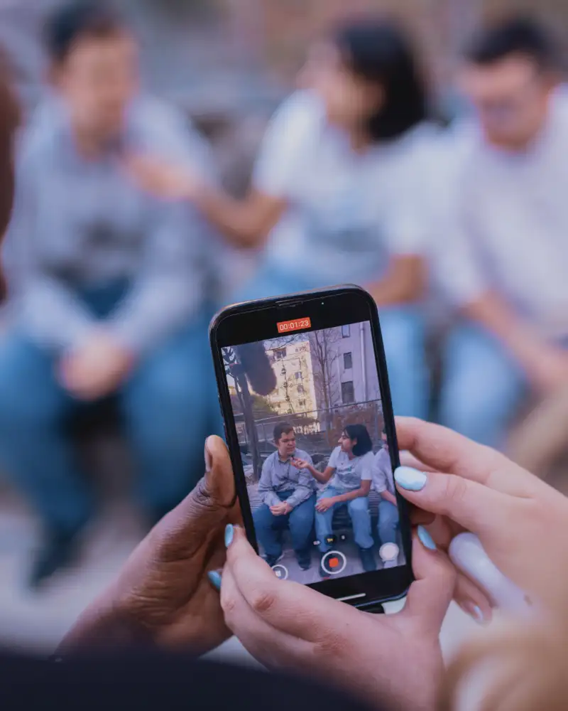 Jugendliche, von denen man nur die Hände sieht, filmen andere Jugendliche in einer Hochhaussiedlung mit dem Smartphone.