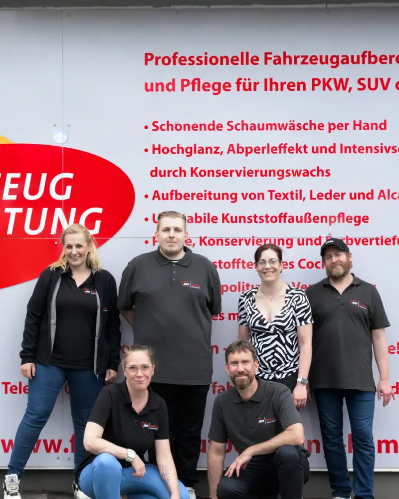 Sechs Personen stehen vor einem großen Plakat. Darauf steht unter anderem: "Fahrzeug Aufbereitung Kamen".