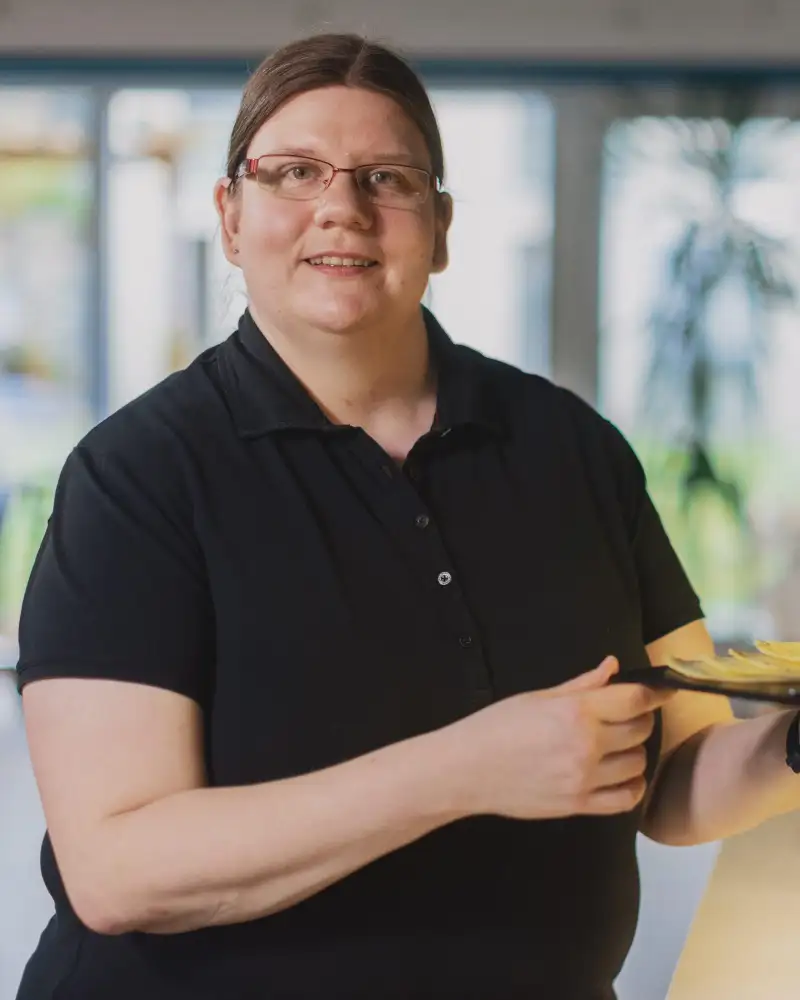 Eine junge Frau stellt einen Teller mit Obst in eine Vitrine.