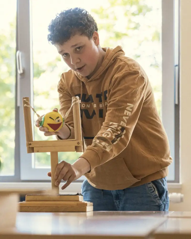 Ein Junge wirft mit einem Ball einen Klötzchenstapel um.