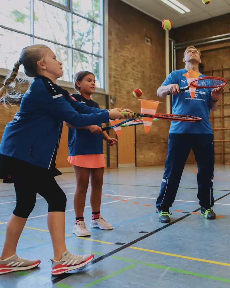 Ein Mann und zwei Mädchen schlagen mit Tennisschlägern Tennisbälle in die Luft.