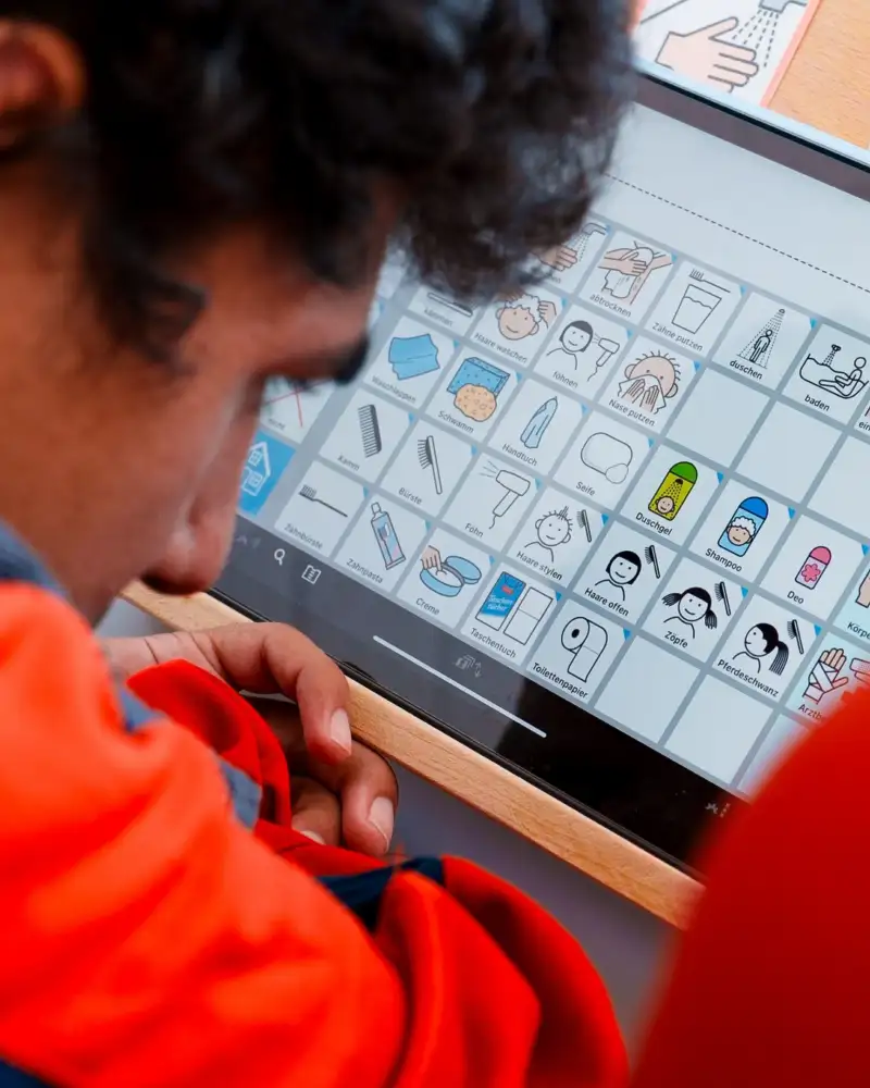 Ein Mann und eine Frau beugen sich nebeneinander über ein Tablet. Sie schauen auf den Bildschirm, auf dem verschiedene Symbole zu sehen sind.