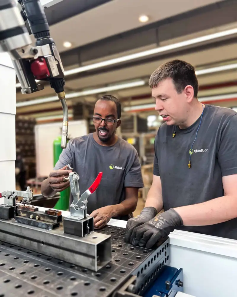 Zwei Männer arbeiten an einem Schweißgerät in einer Werkstatt.