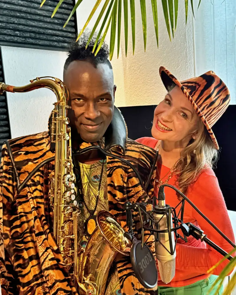 Eine weiße Frau mit Tigerfell-Hut und ein schwarzer Mann mit Tigerkostüm und Saxophon.