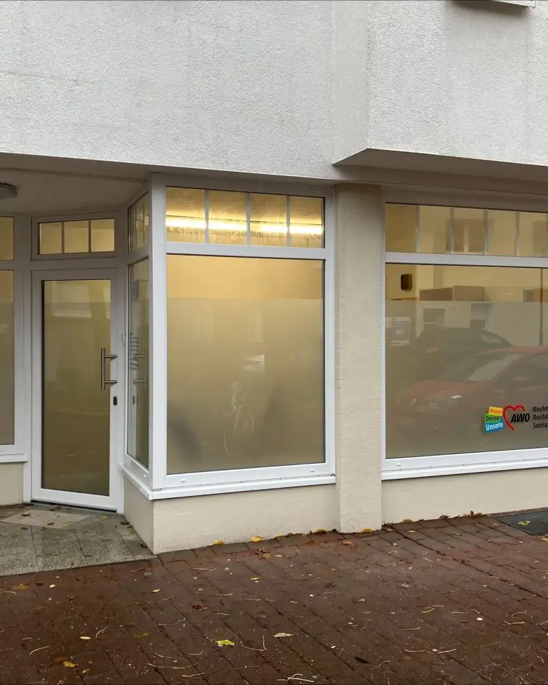 Ein Ladenlokal mit Schaufenstern aus undurchsichtigem Glas und einer Glastür in einem überdachten Eingang. Auf einem der Schaufenster steht: Recht haben Recht bekommen - AWO Sozialberatung.