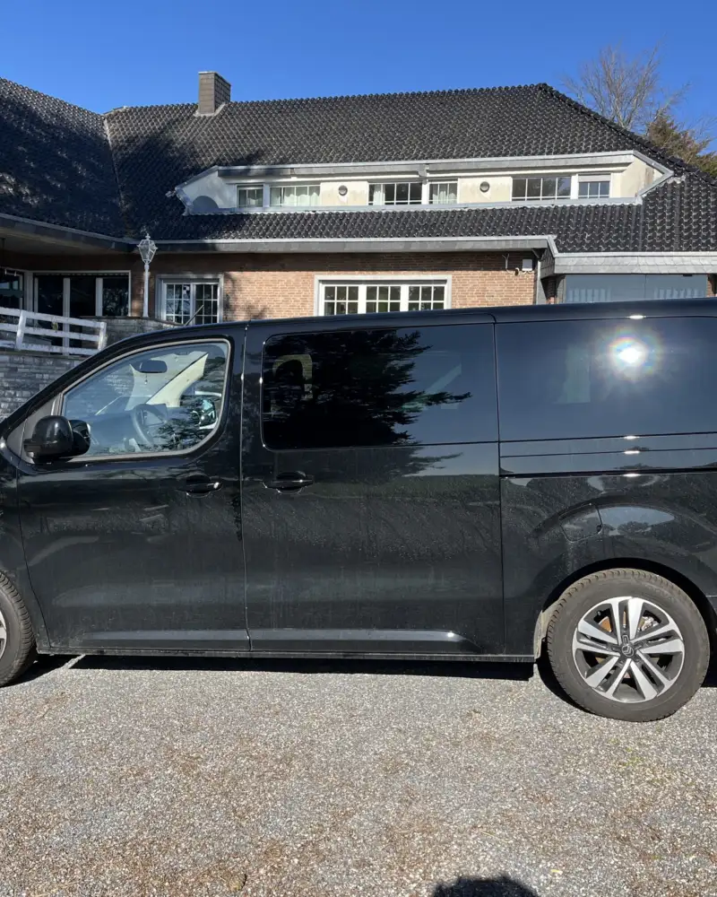 Auf einem Parkplatz steht ein Transporter. Das Fahrzeug ist schwarz, die hinteren Scheiben sind abgedunkelt.