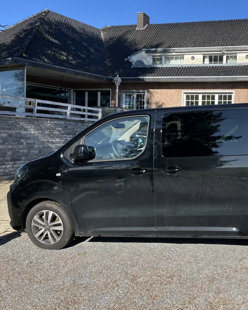 Auf einem Parkplatz steht ein Transporter. Das Fahrzeug ist schwarz, die hinteren Scheiben sind abgedunkelt.