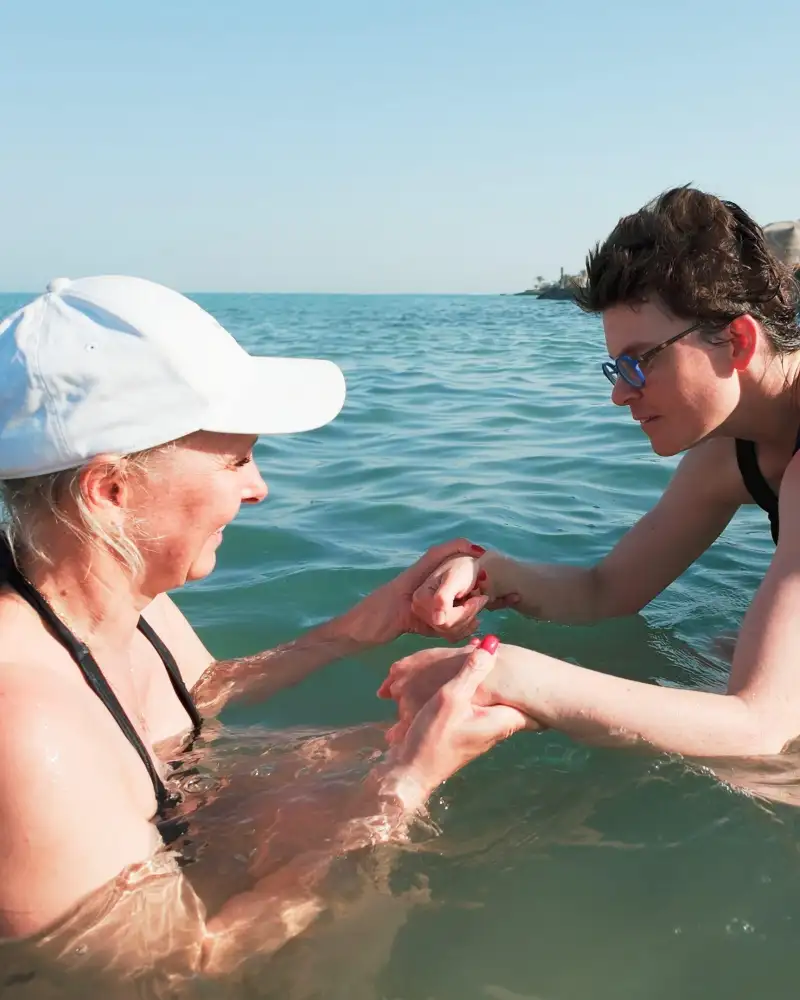 Zwei Frauen in Badeanzügen befinden sich im Wasser, das bis zum Horizont reicht.