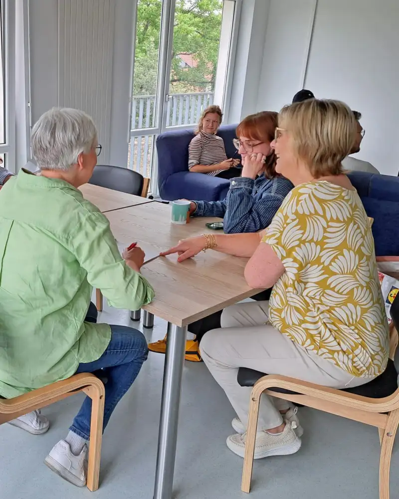 Mehrere Personen sitzen um einen Tisch und auf dem Sofa