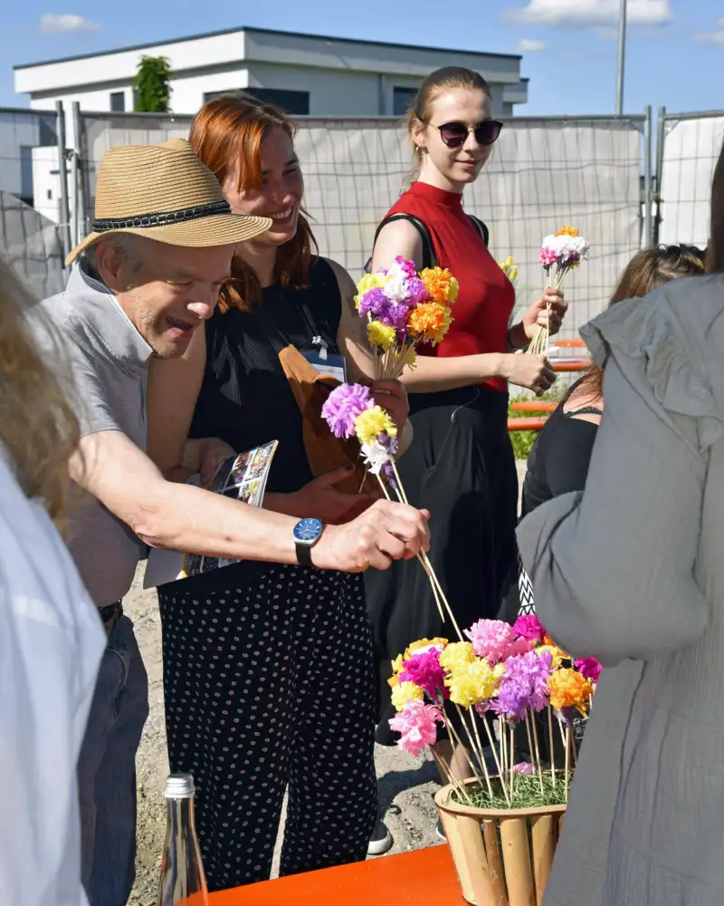 Mehrere Personen stehen an einem Tisch draußen mit Blumen in der Hand.
