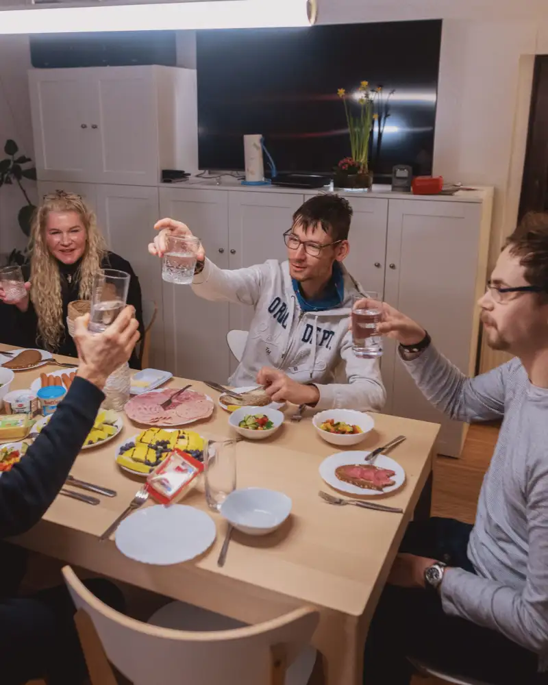 Eine Gruppe junger Menschen sitzt an einem gedeckten Tisch und prostet sich zu.
