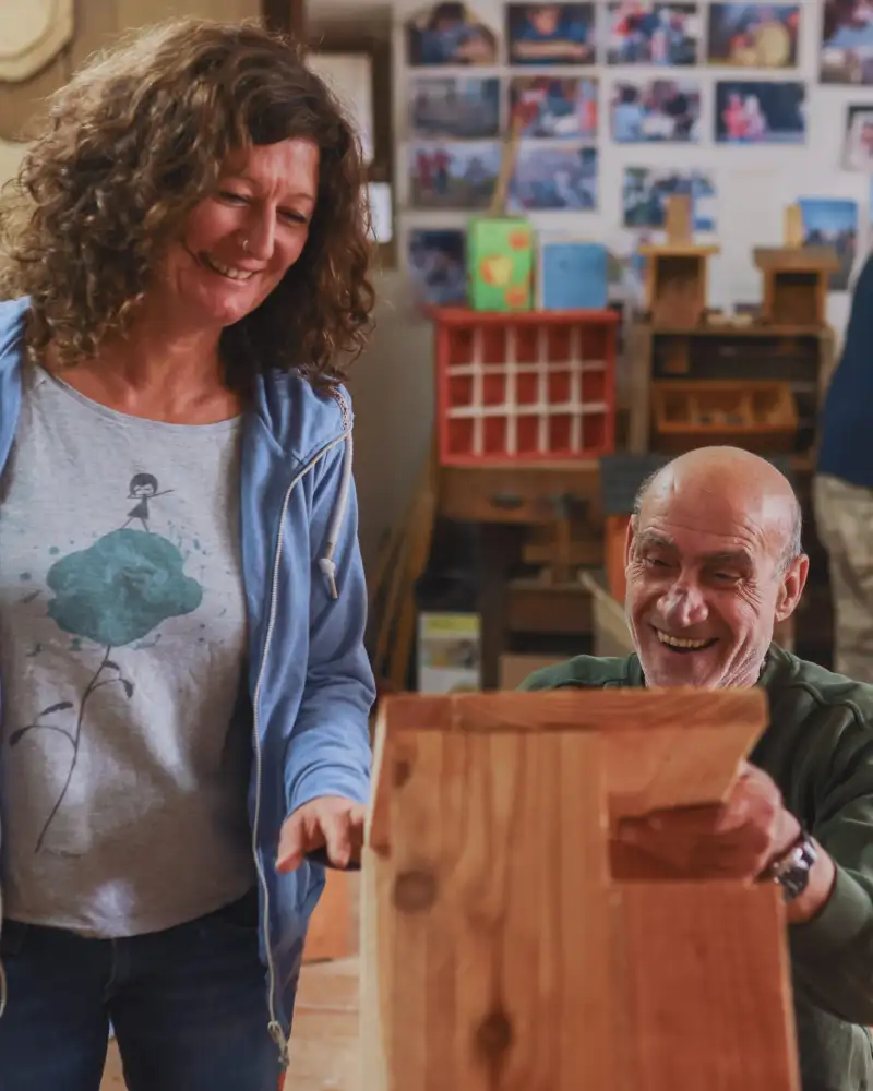 Eine Frau und ein Mann blicken auf einen Kasten aus Holz. Sie lachen.