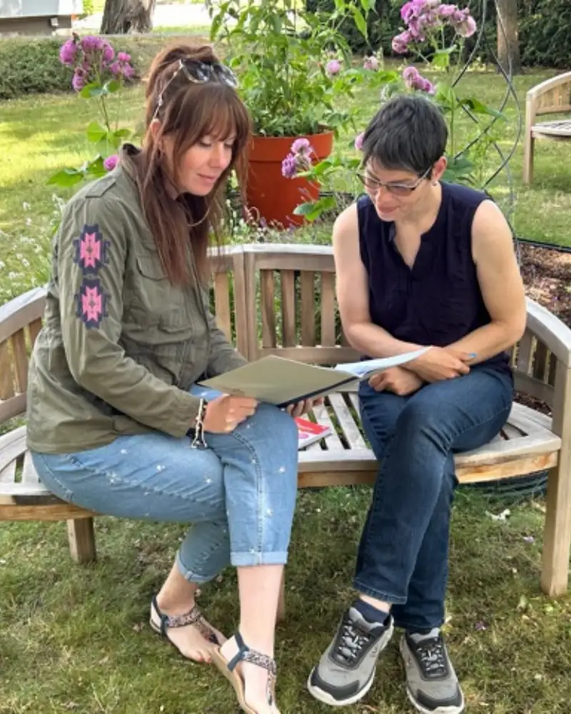 Zwei Frauen sitzen bei einer Besprechung draußen auf einer Gartenbank.