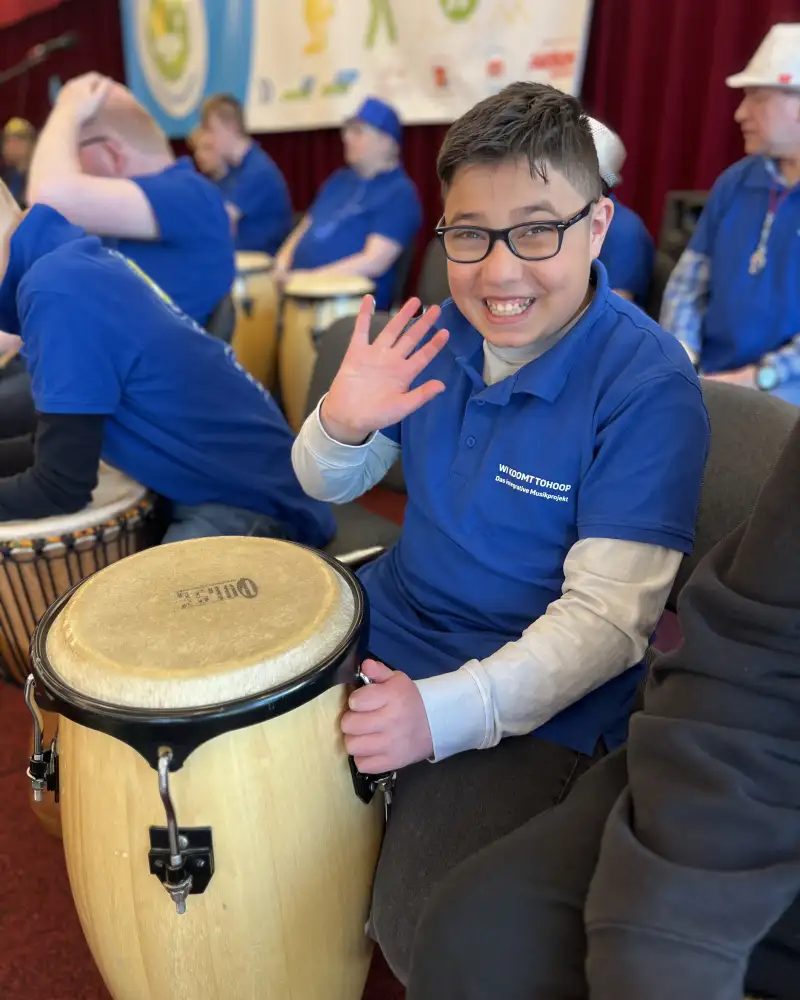 Ein Junge mit einer Trommel winkt in die Kamera.
