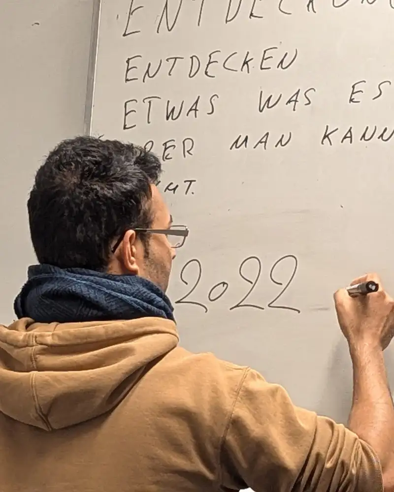 Zwei Männer, die von hinten zu sehen sind, stehen vor einem beschriebenen Flipchart. Einer von beiden schreibt etwas neben die Zahl 2022.