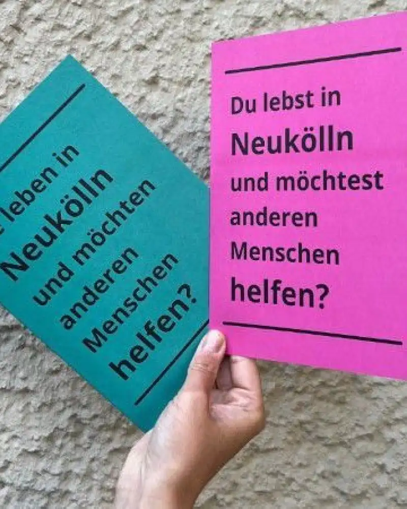 Eine Hand hebt zwei verschiedenfarbige Karten hoch. Auf der pinkfarbenen steht: Du lebst in Neukölln und möchtest anderen Menschen helfen? Auf der grünen Karte steht: Sie leben in Neukölln und möchten anderen Menschen helfen?