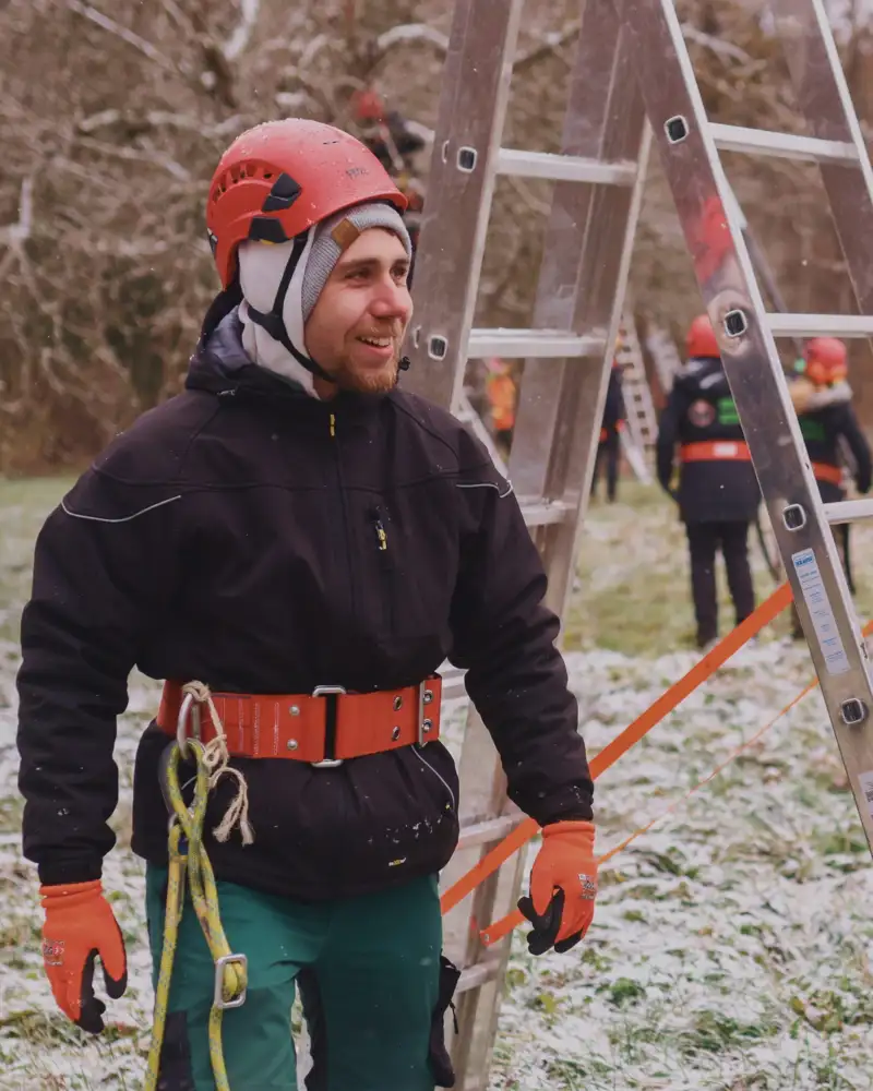 Zwei Männer mit orangefarbenen Schutzhelmen tragen gemeinsam eine Leiter.