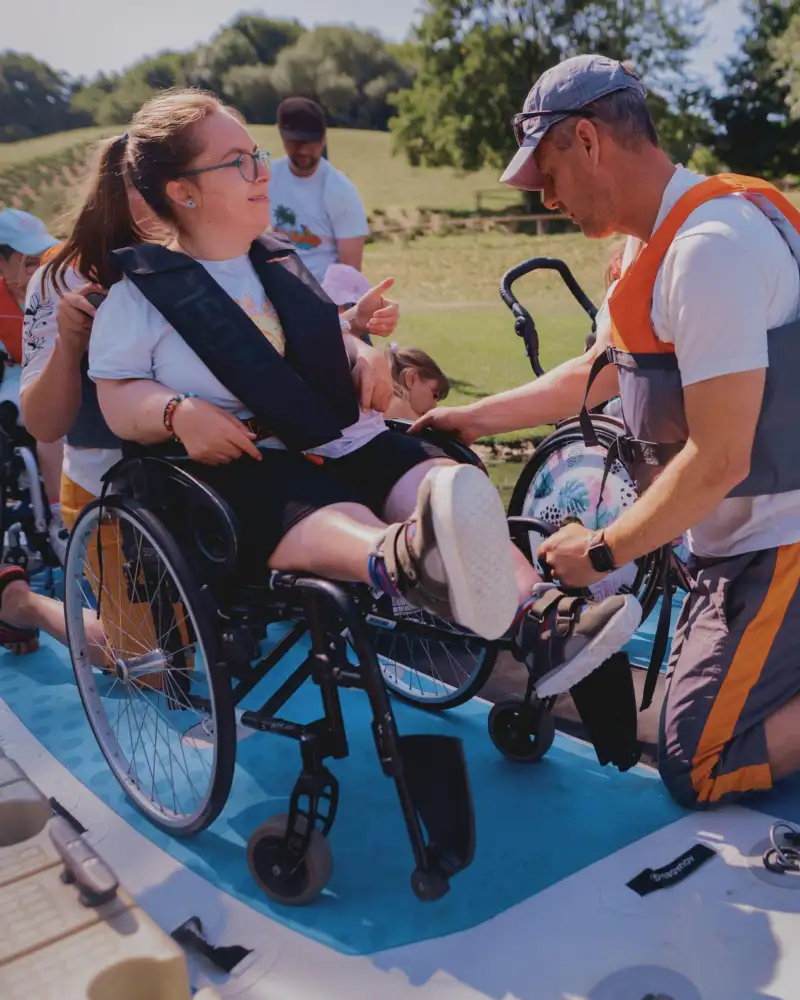 Personen mit und ohne Rollstuhl auf einem grußen Paddel-Board in einem Gewässer