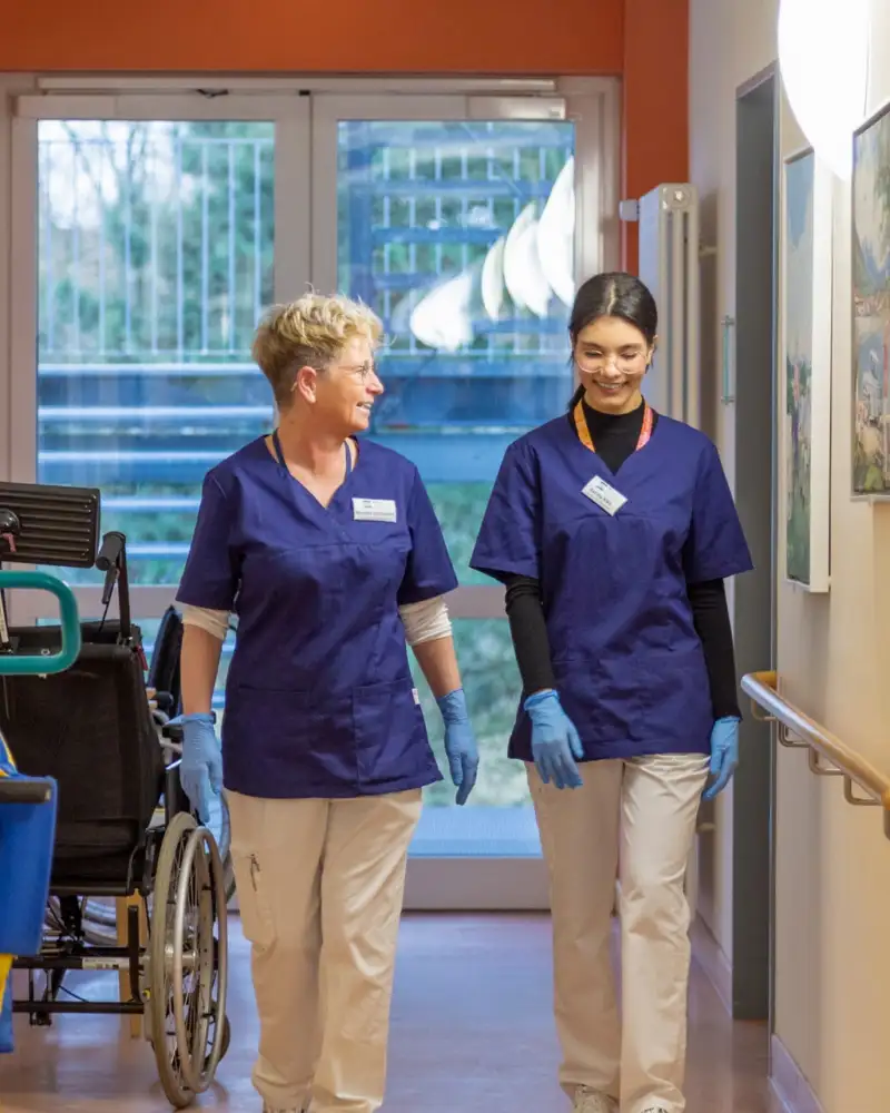 Zwei Frauen in Dienstkleidung im Flur einer Pflegeeinrichtung
