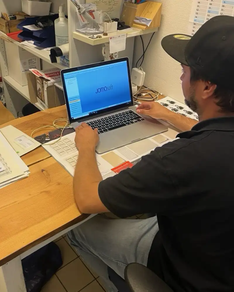 Ein Mann mit Basecap sitzt vor einem aufgeklappten Laptop und tippt auf der Tastatur.