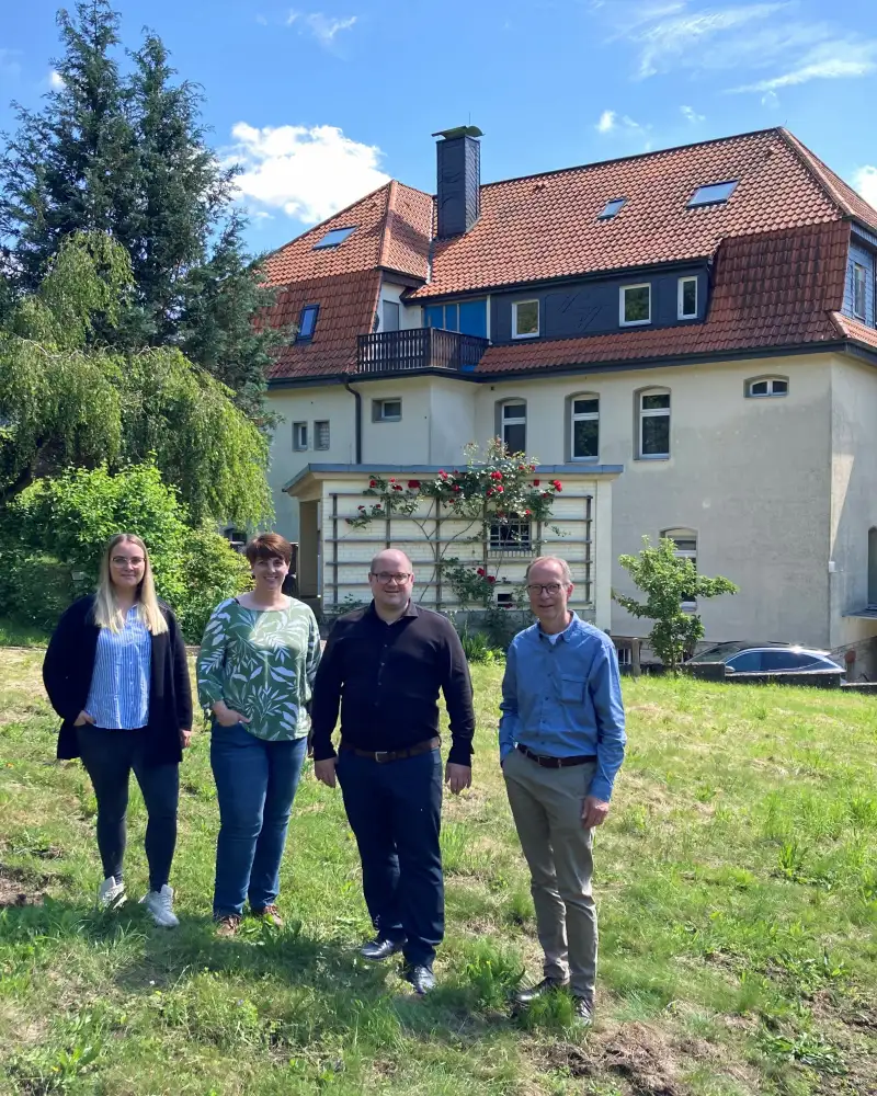 Vier Personen stehen auf einer Wiese vor einem Haus