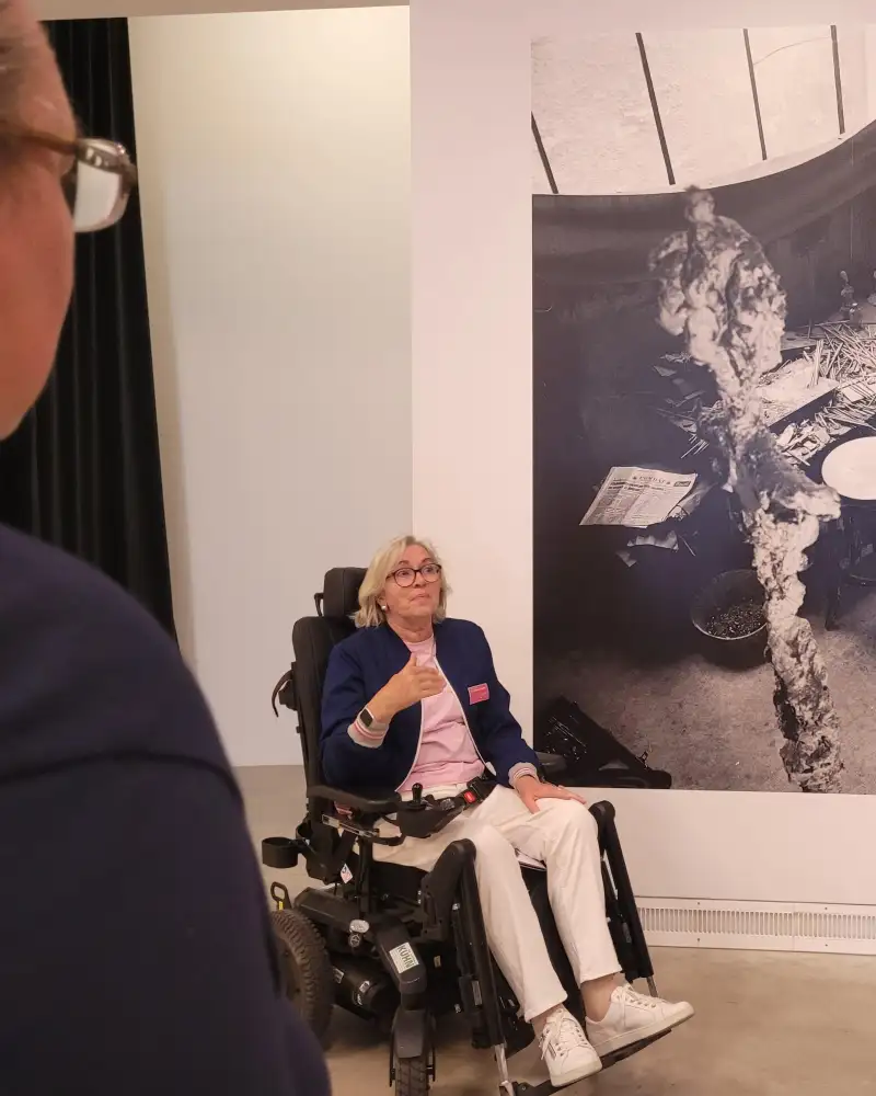 Eine Frau im Rollstuhl vor einem großformatigen Foto in einer Ausstellung
