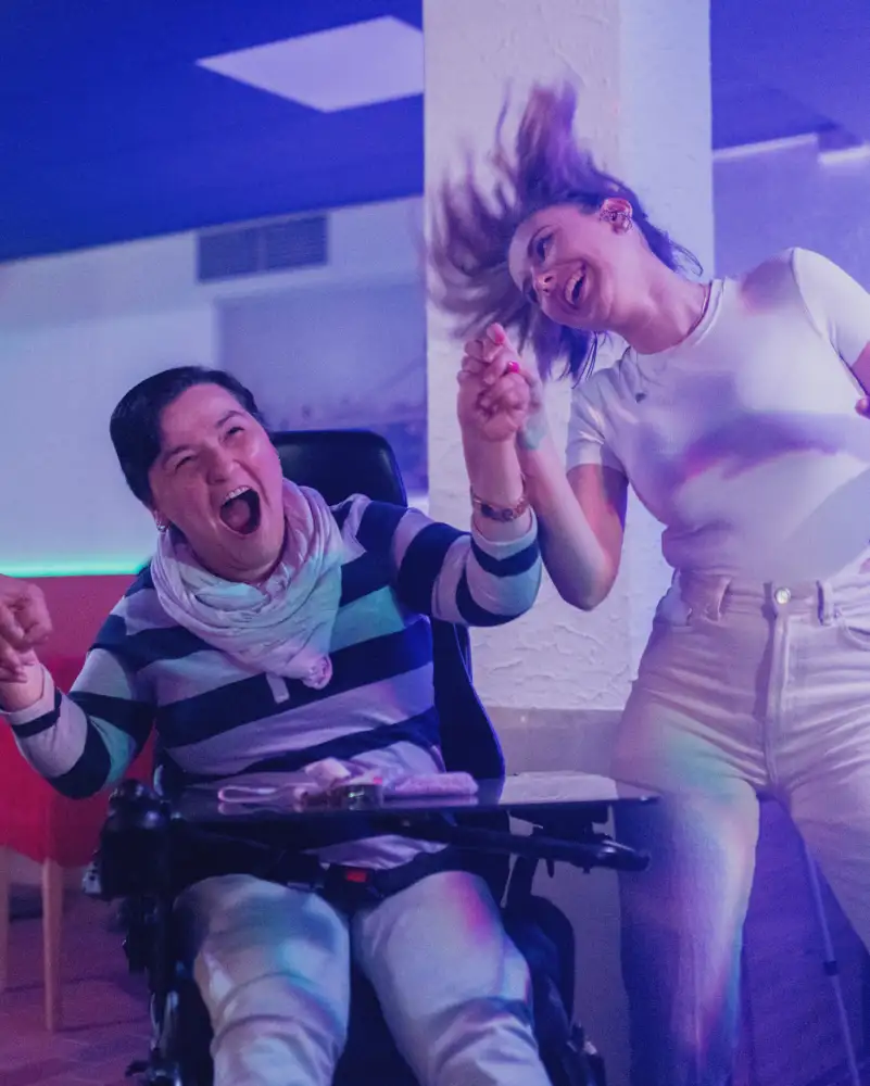 Ein Mann und zwei Frauen in der Disco. Eine von ihnen sitzt im Rollstuhl. Alle drei halten sich an den Händen und bewegen sich ausgelassen zur Musik.