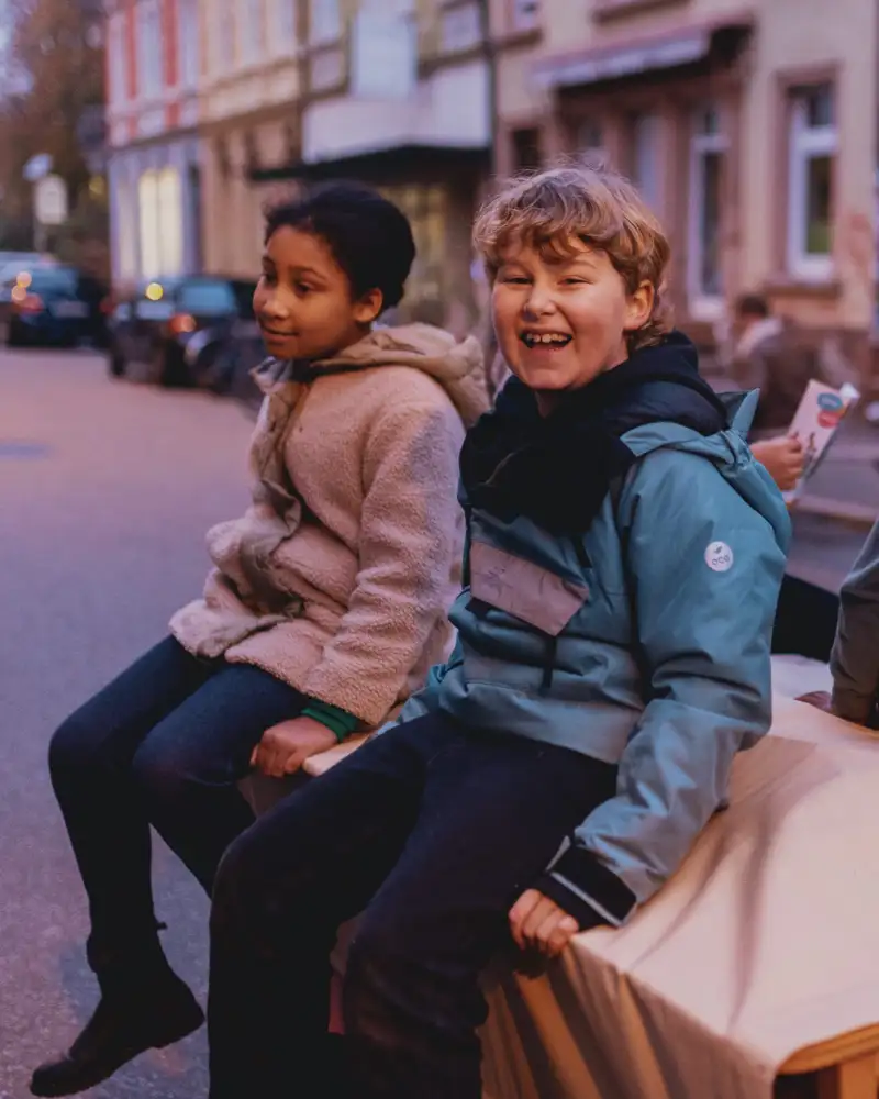 Drei Kinder sitzen im Anhänger eines Lastenrads. Sie lachen.