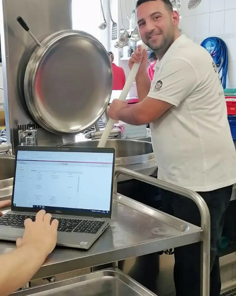Ein Mann am Herd, im Vordergrund ein Laptop