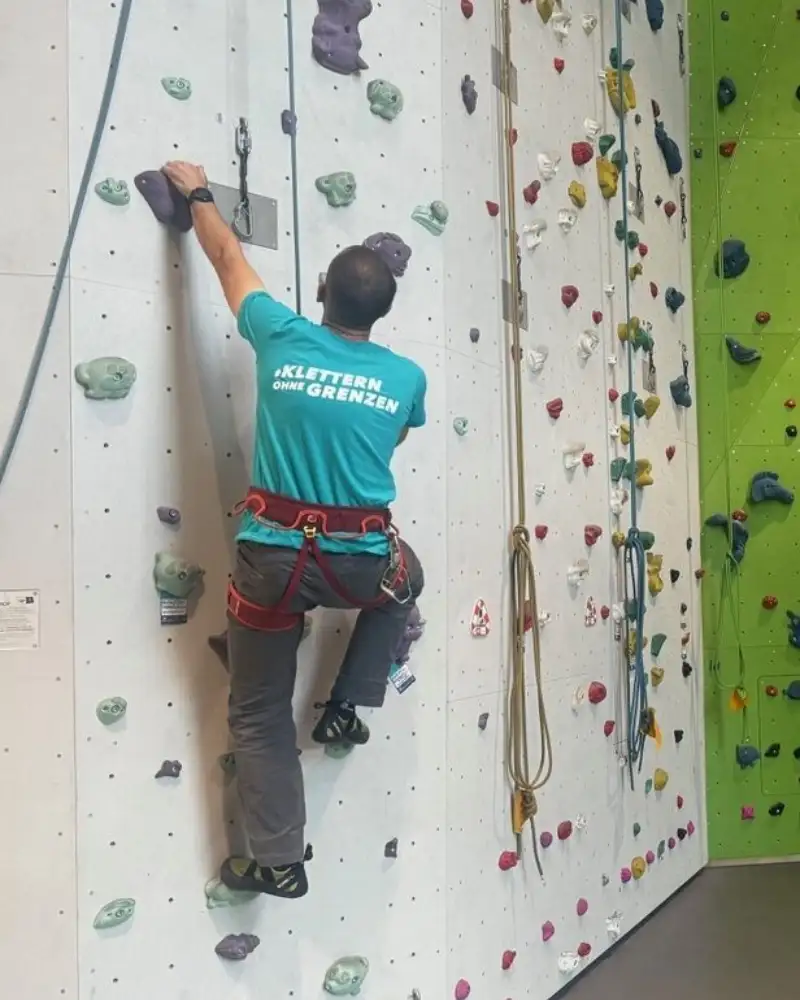 Ein Mann klettert an einer künstlichen Kletterwand hoch. Er ist angeseilt und befindet sich noch relativ weit unten.
