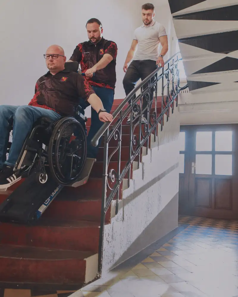 Ein Rollstuhlfahrer auf einer Treppenraupe und weitere Personen auf der Treppe