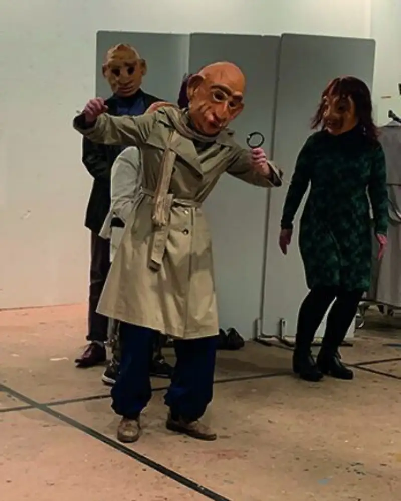 Mehrere Personen mit grußen Masken gestikulieren auf einer Probebühne.