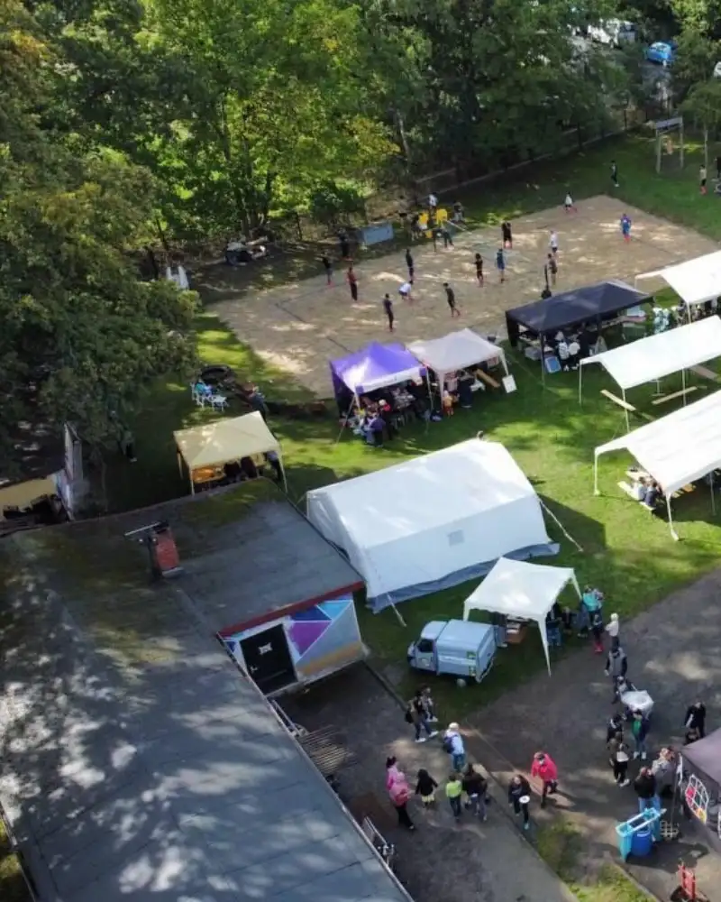 Blick von oben auf eine Sportanlage mit einem festen Gebäude und Freiflächen, auf denen zum Teil verschiedene Zelte aufgebaut sind.