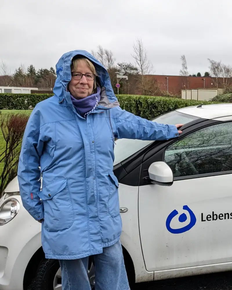 Zwei Männer in Parkas lehnen an einem weißen Wagen mit der Aufschrift Lebenshilfe Husum.