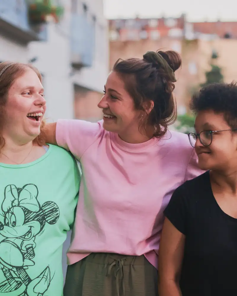 Zwei junge Frauen und ein Mädchen stehen lachend Arm in Arm im Freien