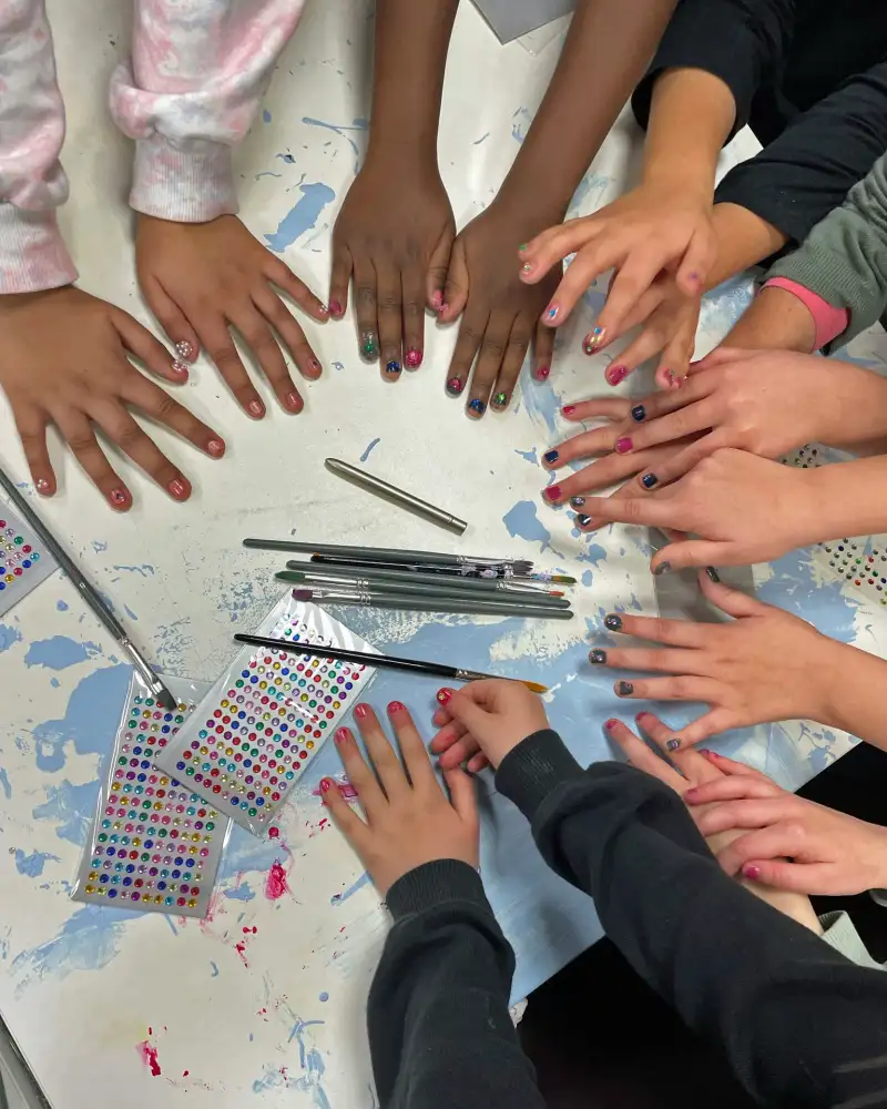 Viele ausgestreckte Kinderhände auf einem Basteltisch mit teils bunten Fingernägeln.