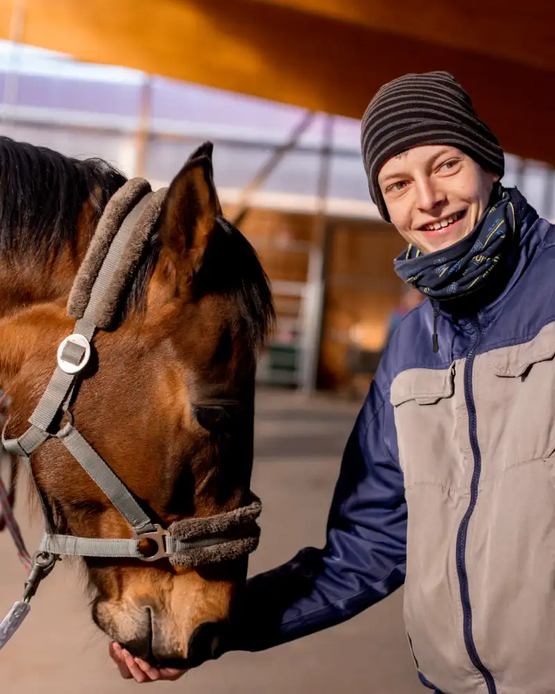 Ein Pferd frisst einem jungen Mann aus der Hand.