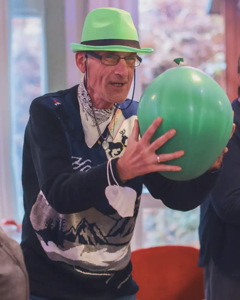Ein Mann mit grünem Hut und grünem Ball umringt von anderen Menschen