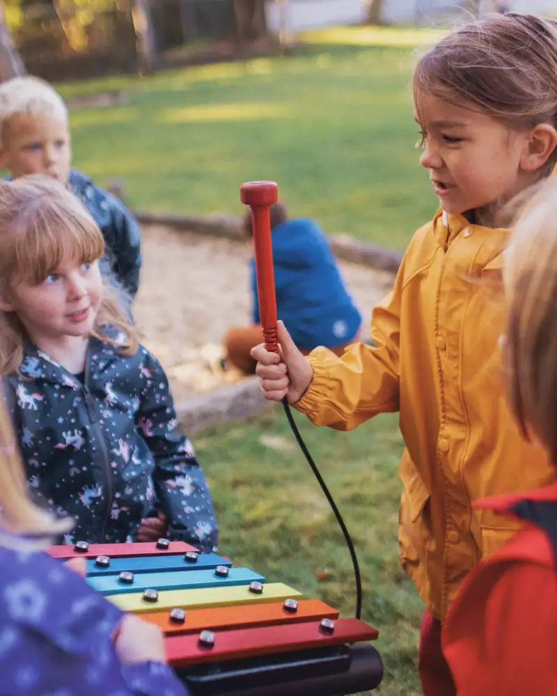 Mehrere Kindergartenkinder spielen draußen mit Klanginstrumenten