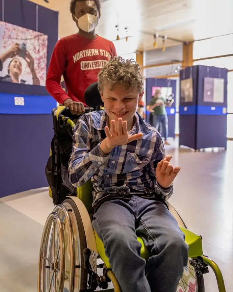 Ein Junge im Rollstuhl wird in einer Ausstellung geschoben