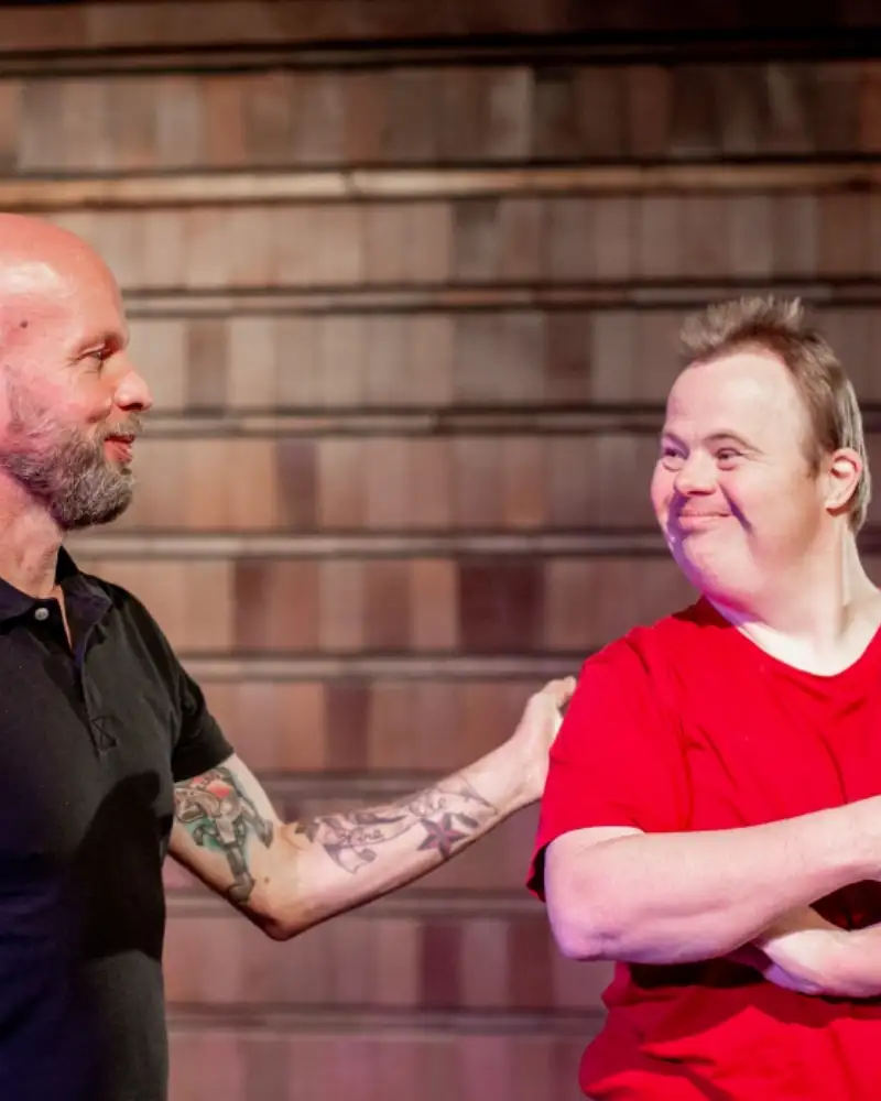 Zwei Männer auf einer Bühne, einer von ihnen hat das Downsyndrom.