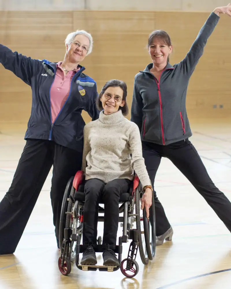Drei Frauen, eine davon im Rollstuhl, bilden eine Tanzformation.