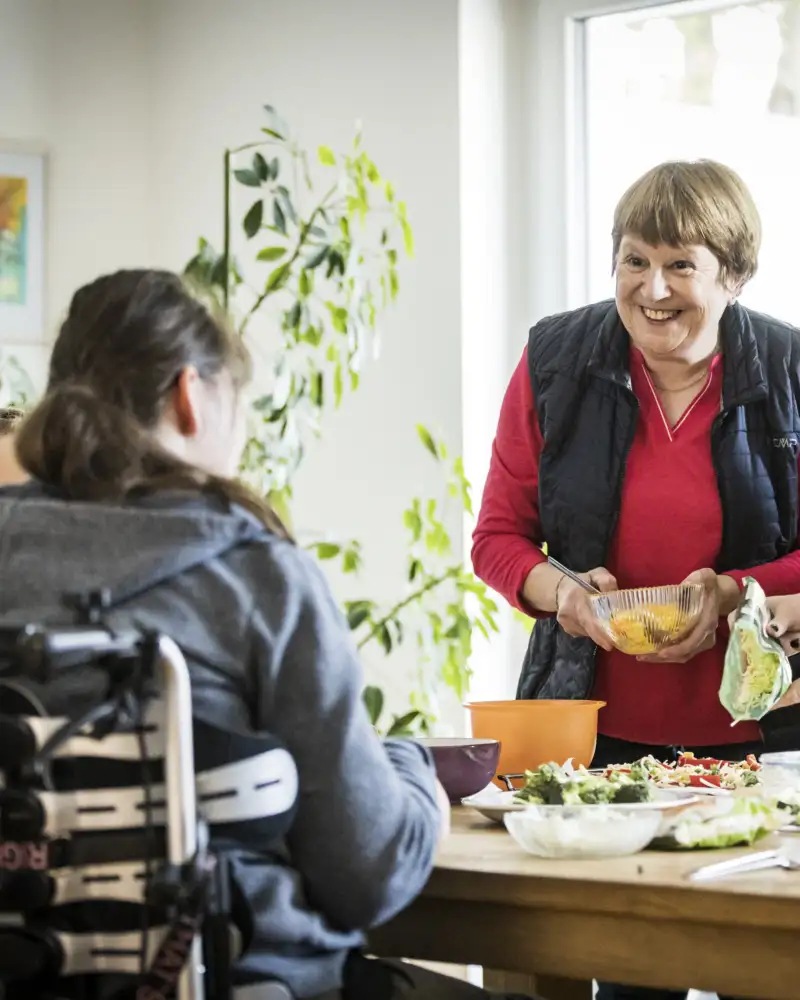 Mehrere Personen stehen und sitzen rund um einen Tisch in einer Wohnung