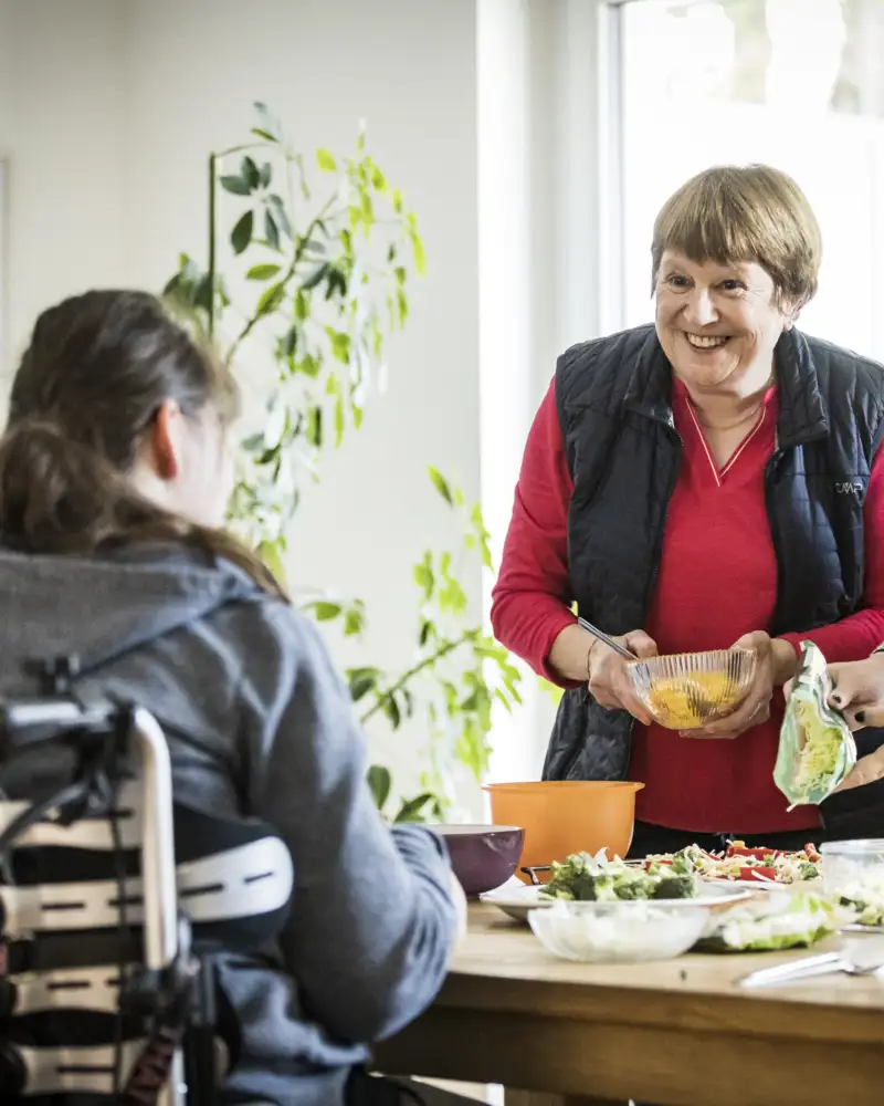 Mehrere Personen stehen und sitzen rund um einen Tisch in einer Wohnung