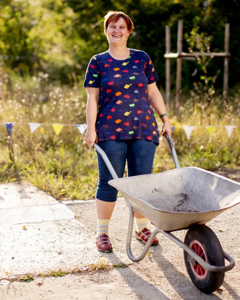 Eine Frau mit einer Schubkarre in einem Garten.